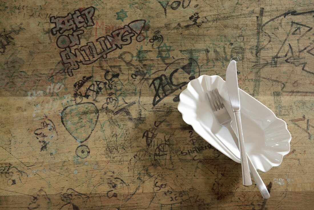 White ceramic hot dog tray on wooden table covered in graffiti