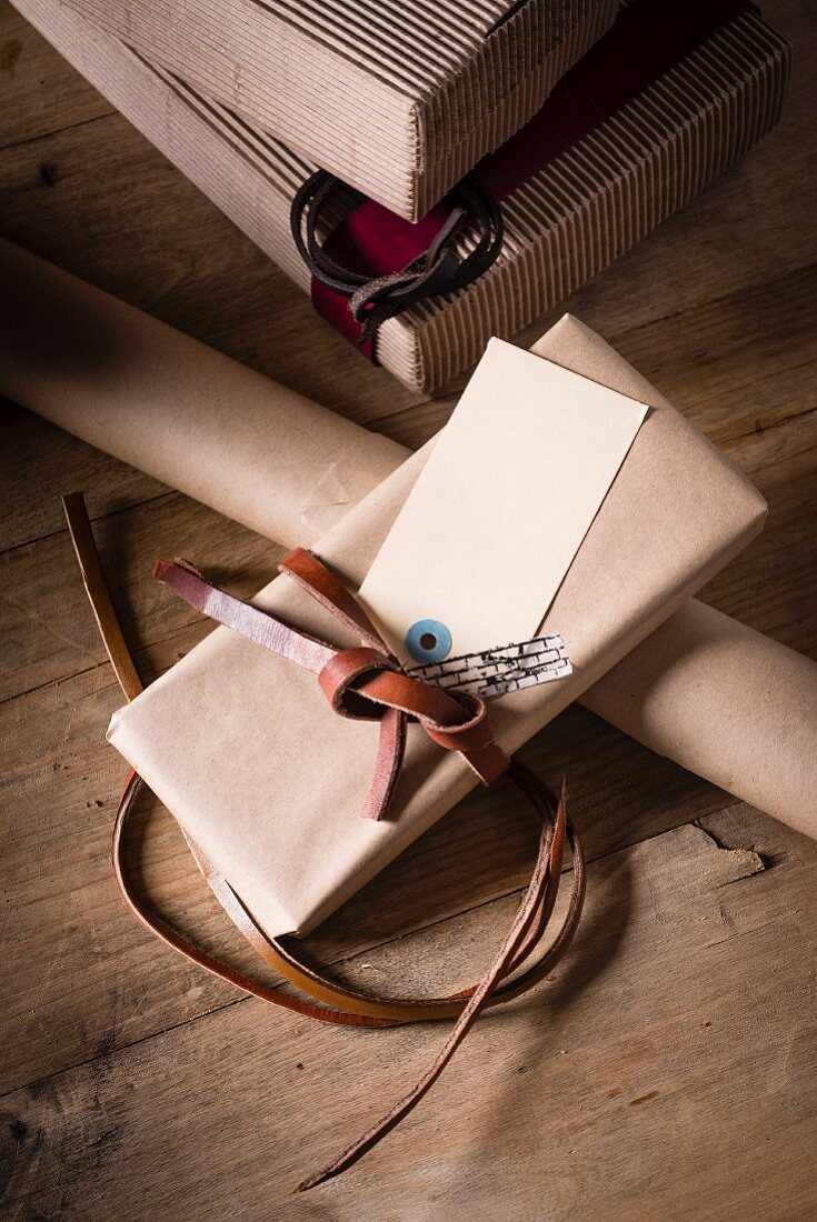 Geschenkschachteln, Geschenkpapier und verpacktes Geschenk mit Lederband auf Holztisch