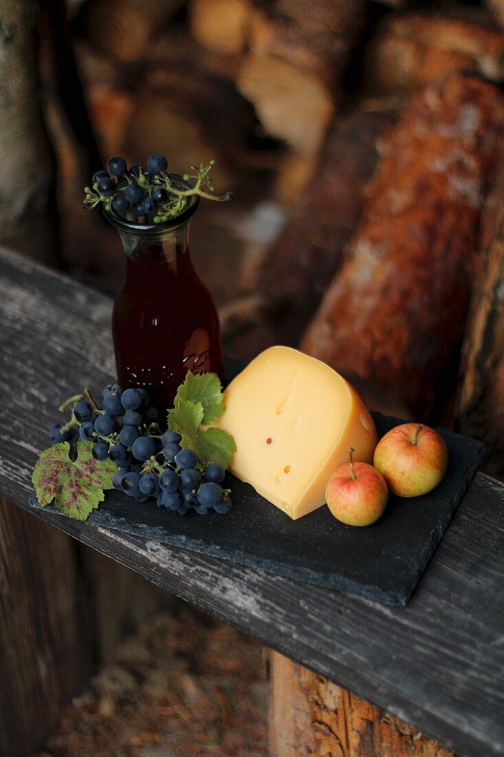 Käse, Äpfel und Trauben auf Holzbrett im Garten