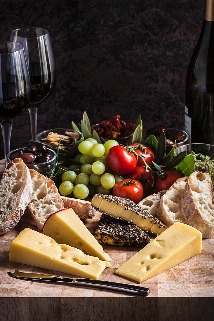 A cheese platter with bread, spices, grapes, tomatoes and wine