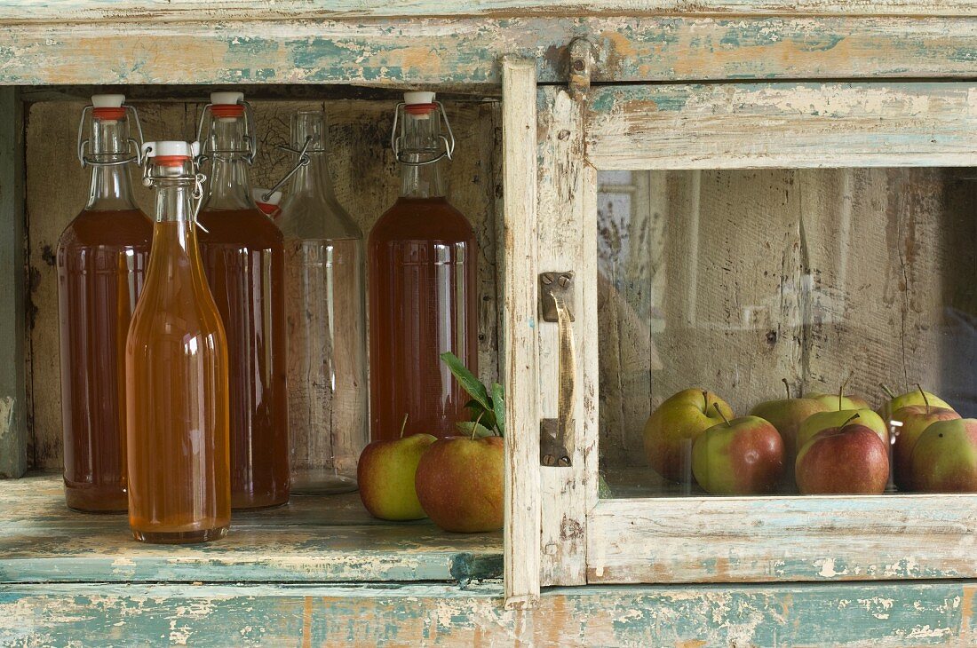 Several bottles of apple juice and apples (variety 'Jonagold') in rustic cupboard