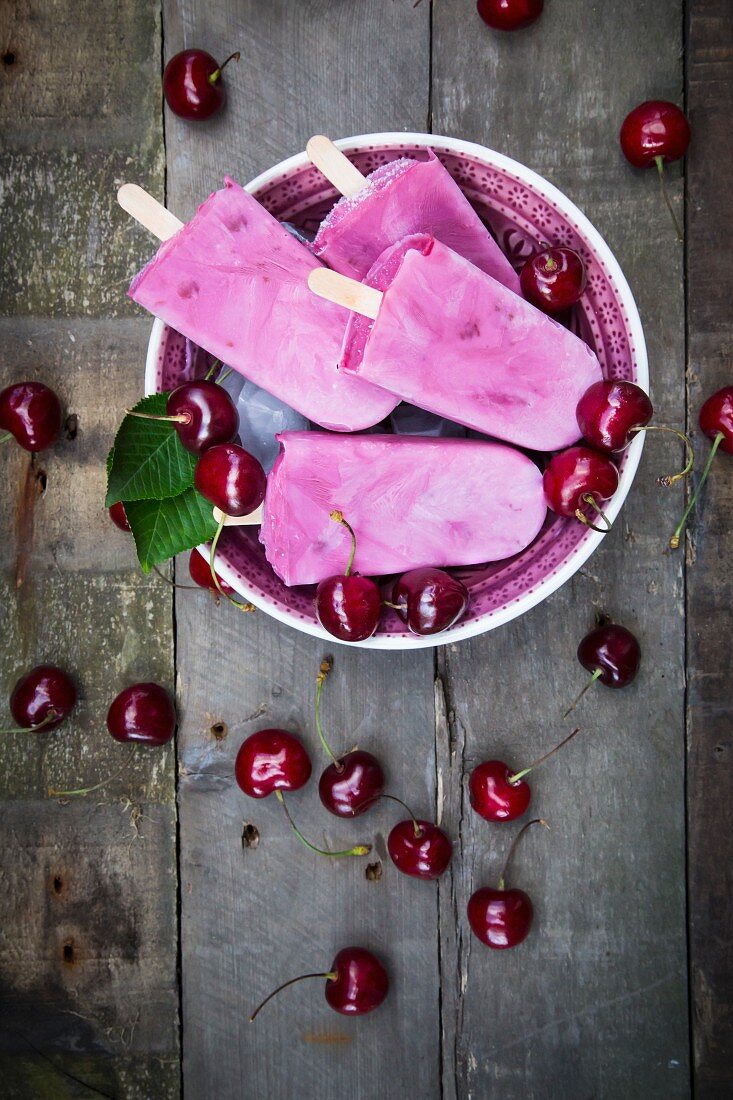 Homemade cherry yoghurt ice cream sticks in a bowl on a wooden surface