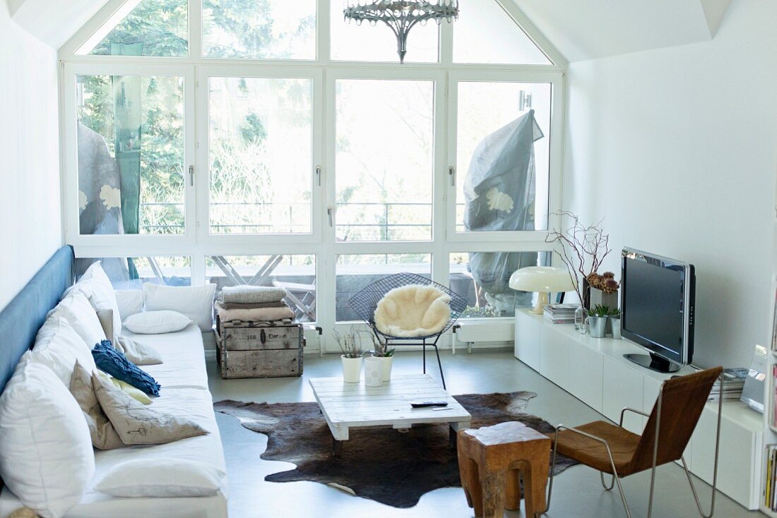 White, modern living room with glass wall leading to balcony