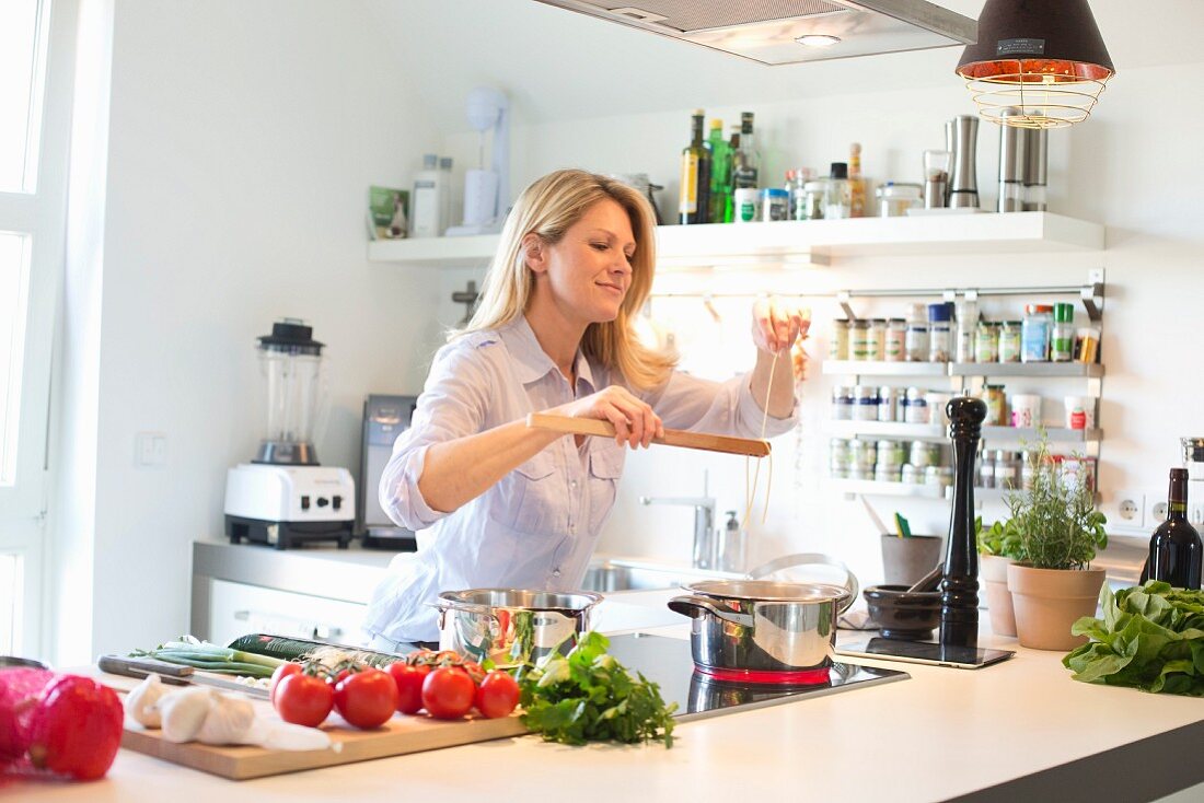 Frau beim Kochen von Spaghetti in moderner Küche