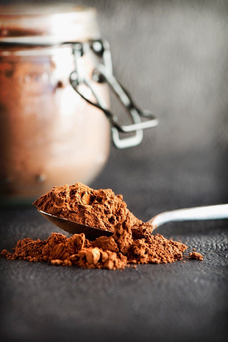 A teaspoon of cocoa powder with a preserving jar in the background