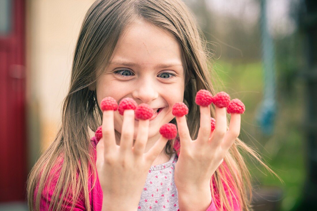 A grinning little girl with raspberries on her fingers
