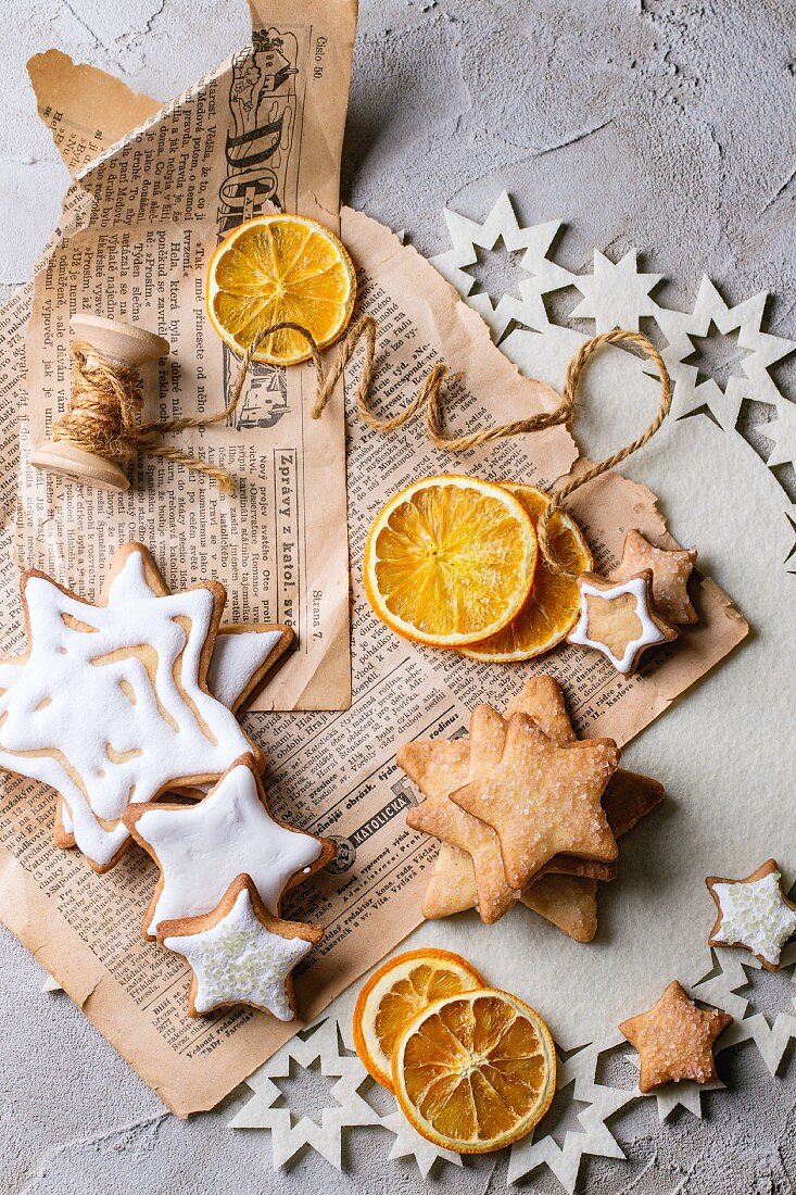 Glasierte Weihnachtsplätzchen in Sternform und getrocknete Orangenscheiben auf alter Zeitung