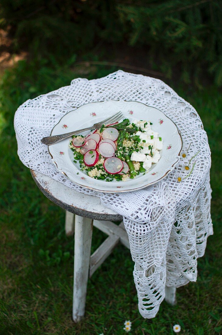 Hirsesalat mit Spargel, Ziegenkäse, Radieschen und Schnittlauch auf altem Gartenstuhl