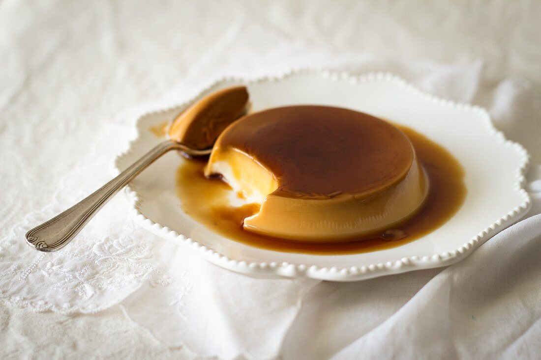 Creme caramel on a plate with a spoon with a bite taken out
