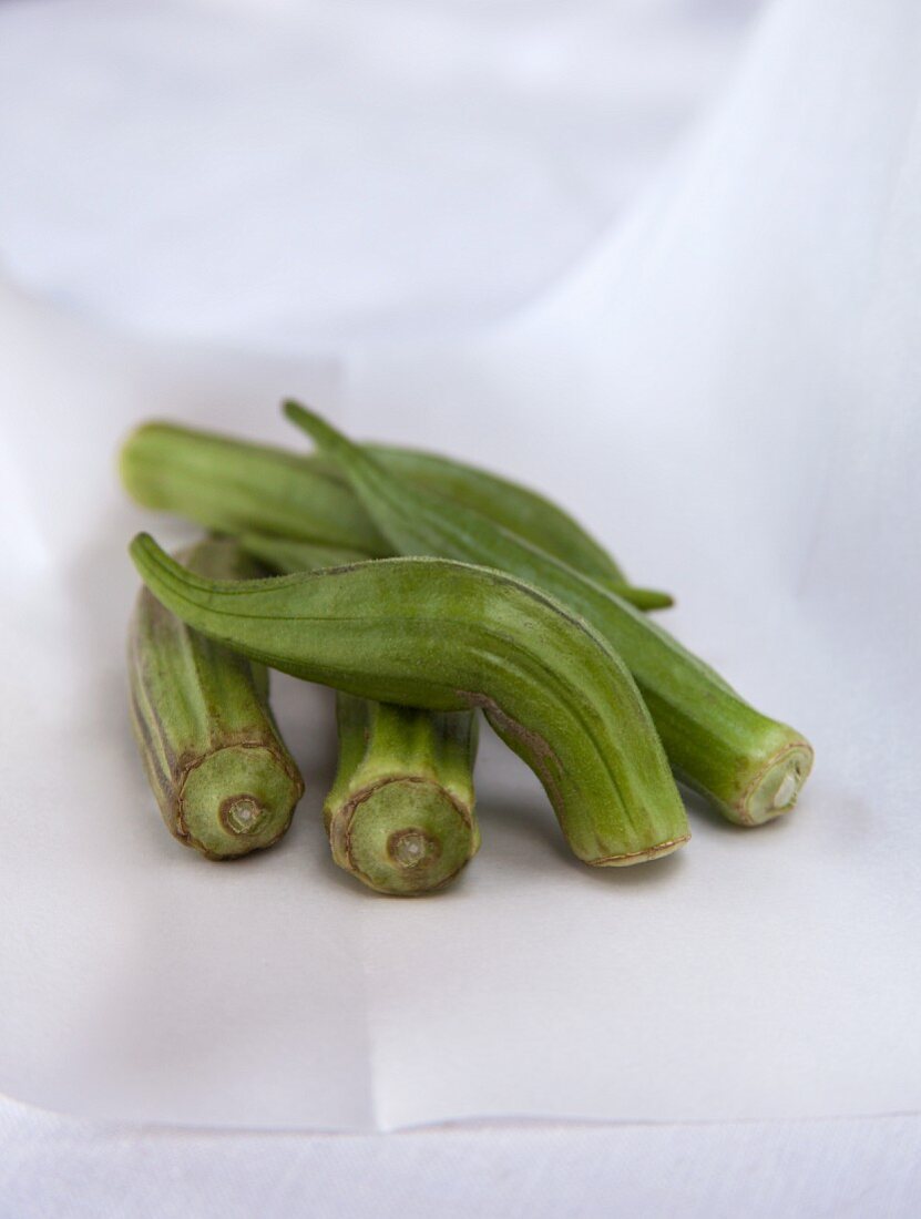 Fresh okra pods on white parchment paper