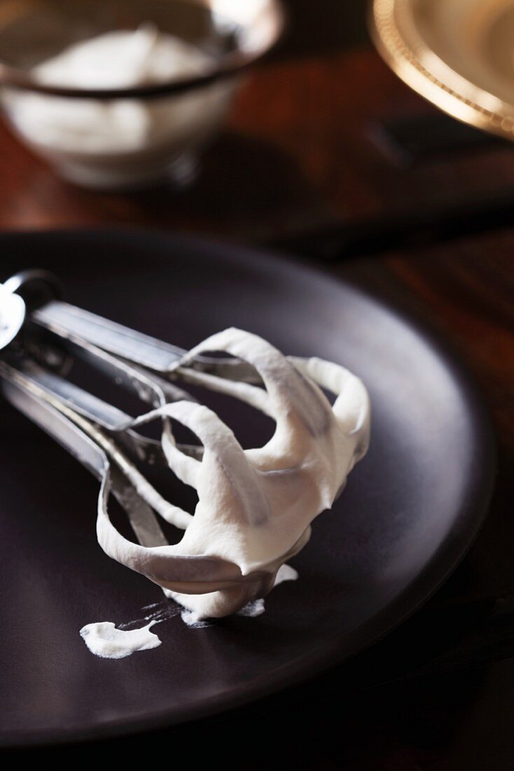 Whisks with freshly whipped cream on a wooden plate