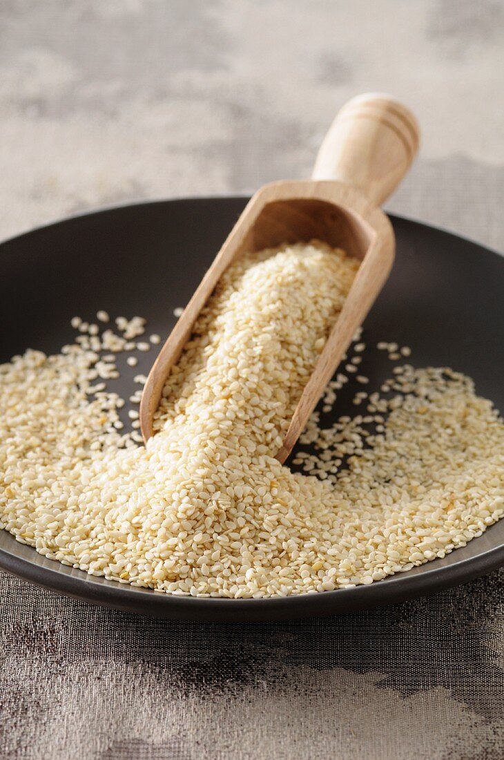 A plate of sesame seeds with a wooden scoop