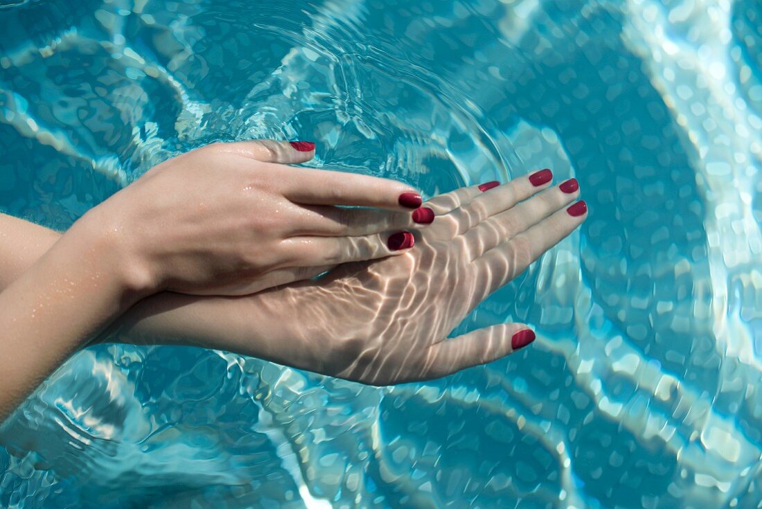 Frauenhände mit rot lackierten Fingernägeln im Wasser