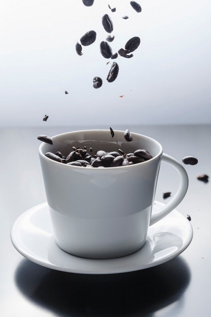 Coffee beans falling into a white coffee cup