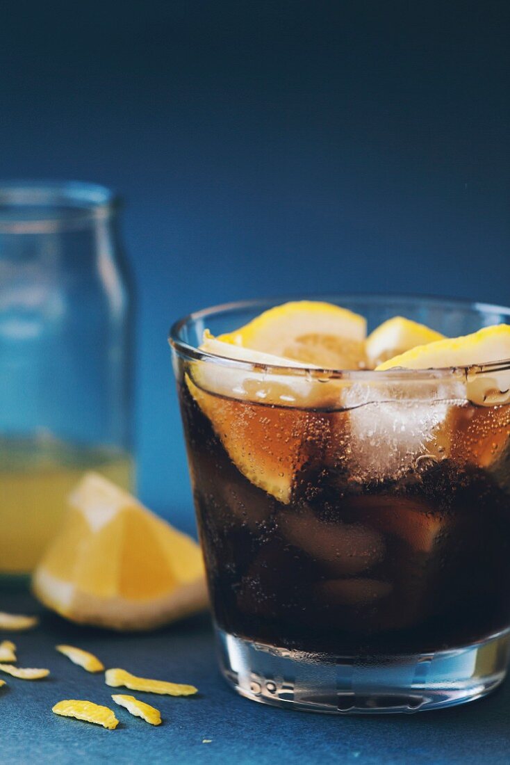 A Cuba Libre with ice cubes and lemon wedges