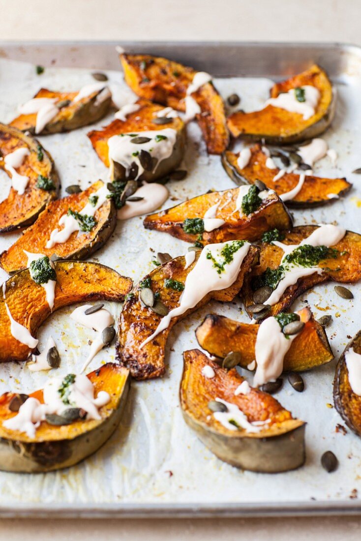 Roasted pumpkin wedges with mayonnaise, pesto and pumpkin seeds on a baking tray