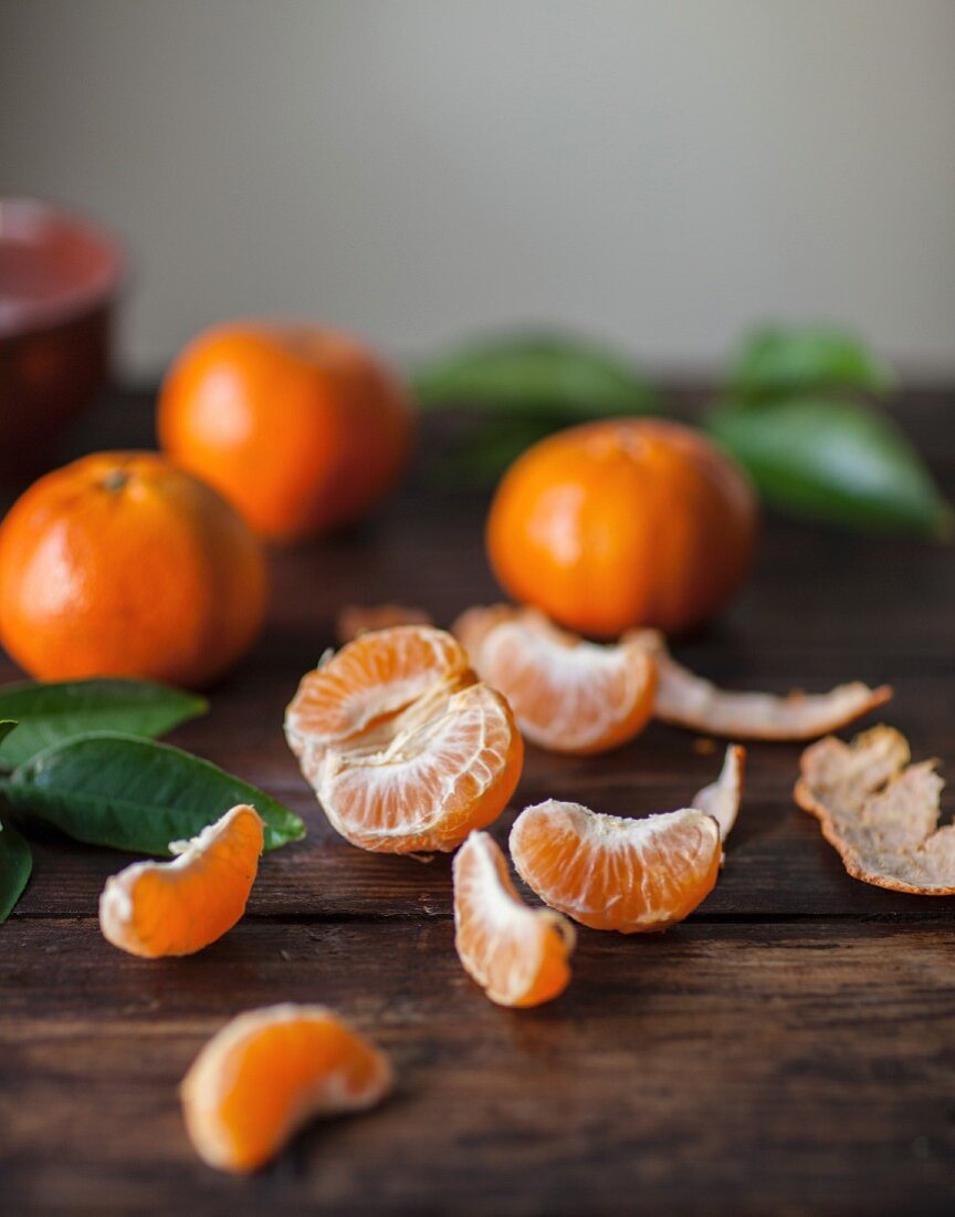 Clementines on a wooden surface, one peeled and split into segments
