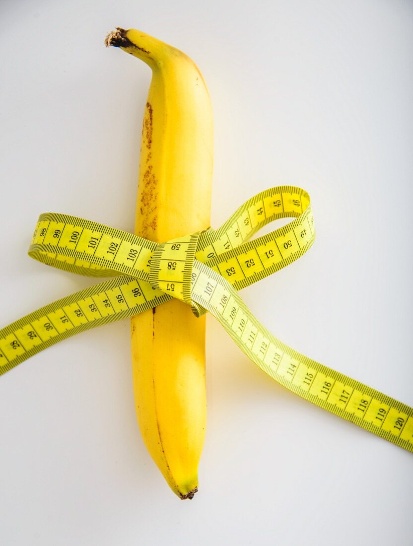 A banana tied with a tape measure on a white surface