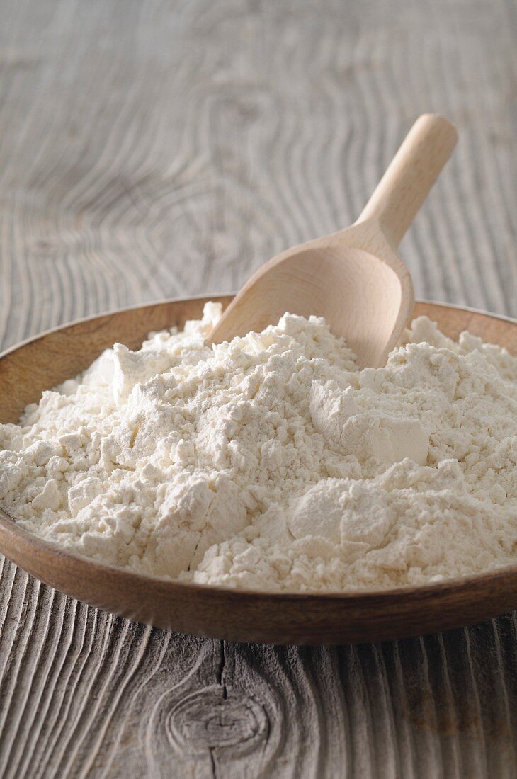 Flour in a wooden bowl with a wooden scoop