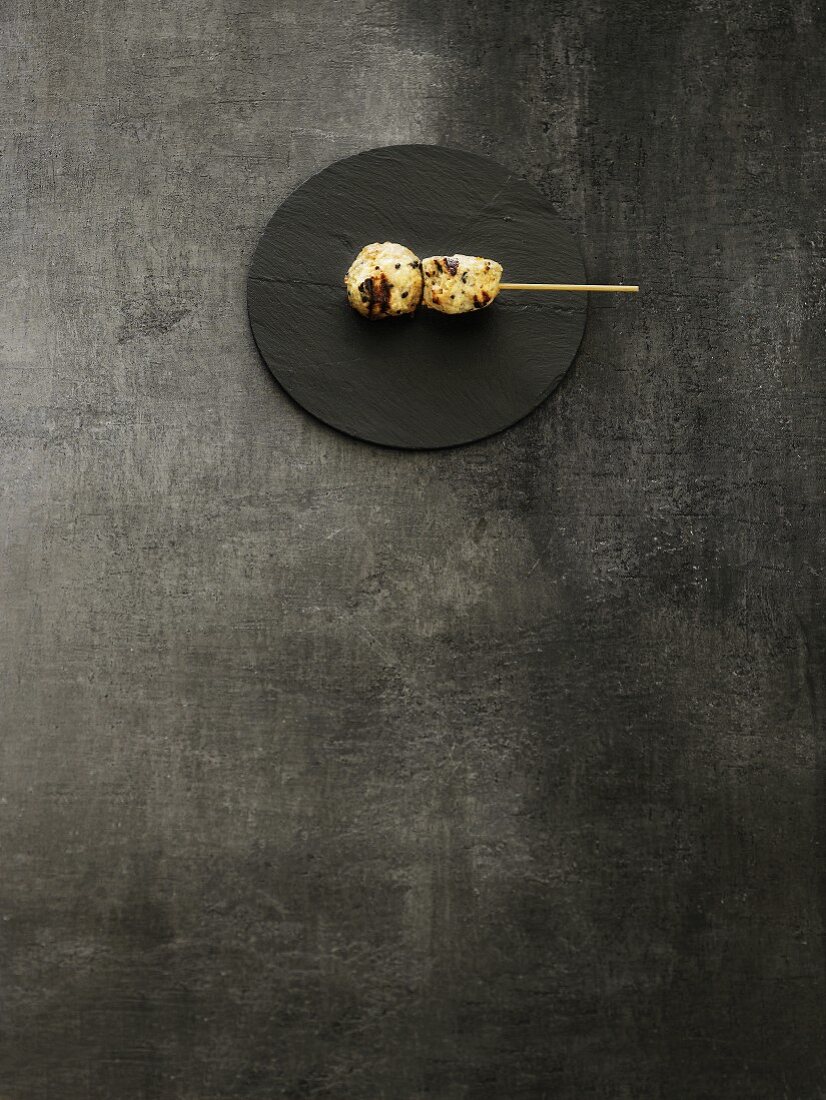 Grilled meat kushi on a wooden stick on a round slate platter