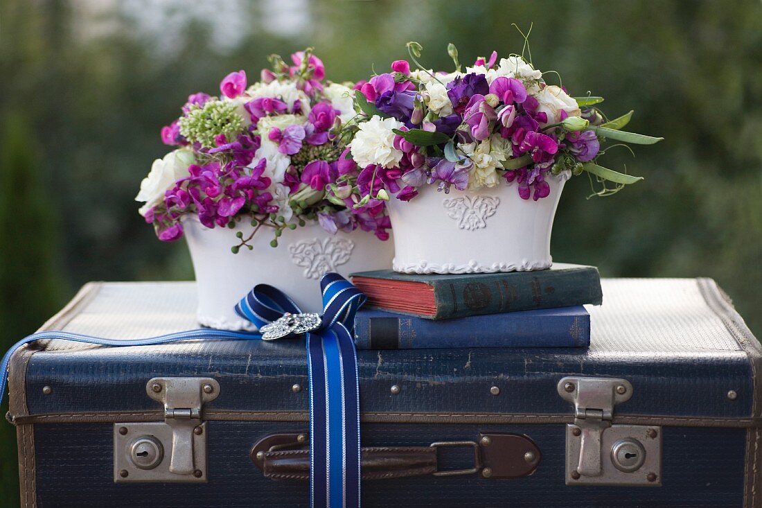 Two romantic flower arrangements and antiquarian books on vintage suitcase decorated with ribbon