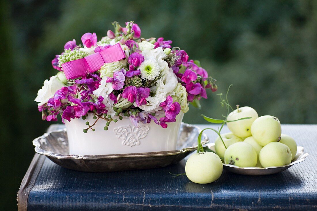 Romantische Blumengesteck mit Äpfeln und Silberschale auf Vintage Koffer im Freien