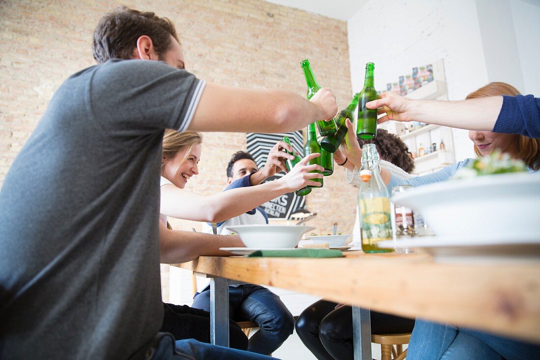 Gemeinsames Essen mit Freunden: Anstossen mit Bierflaschen