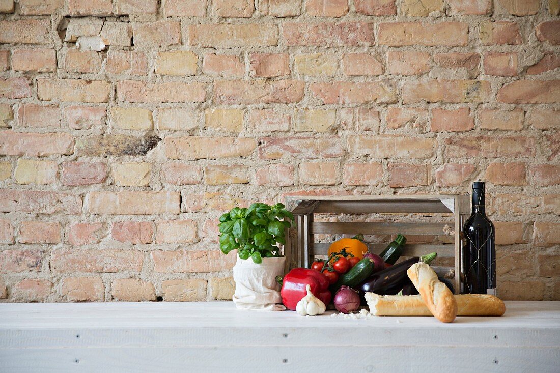 Stillleben mit frischem Gemüse, Basilikum, Rotwein & Baguette vor Steinmauer