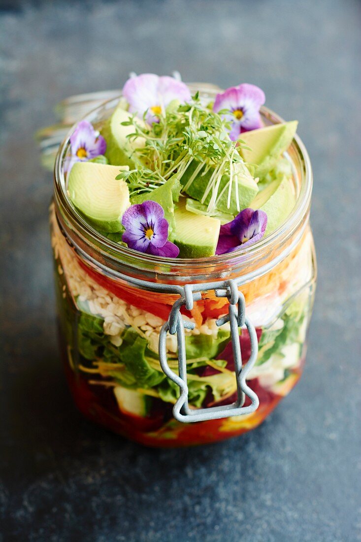 A mixed leaf salad with avocado and edible flowers in a flip-top jar to takeaway