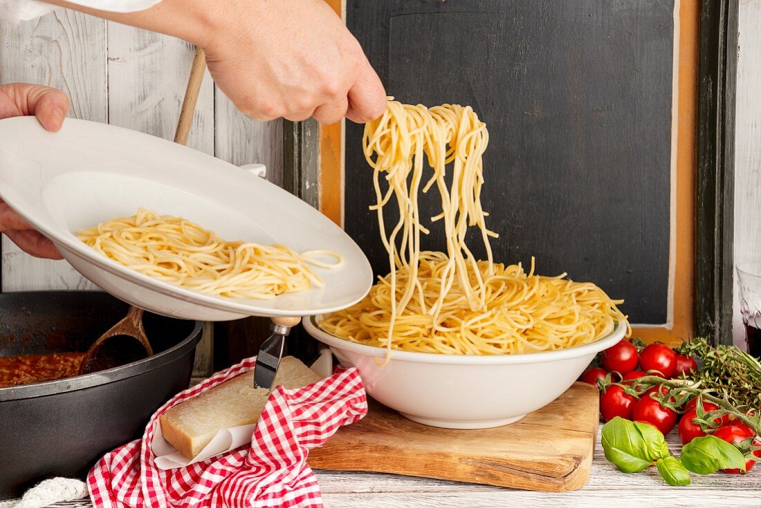 Person füllt gekochte Spaghetti für Spaghetti Bolognese auf Teller