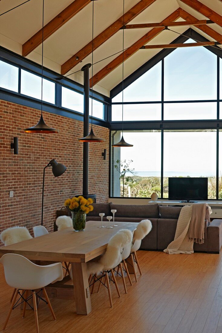 Open-plan interior with exposed wooden structure, brick wall, dining area with classic chairs and solid wooden table