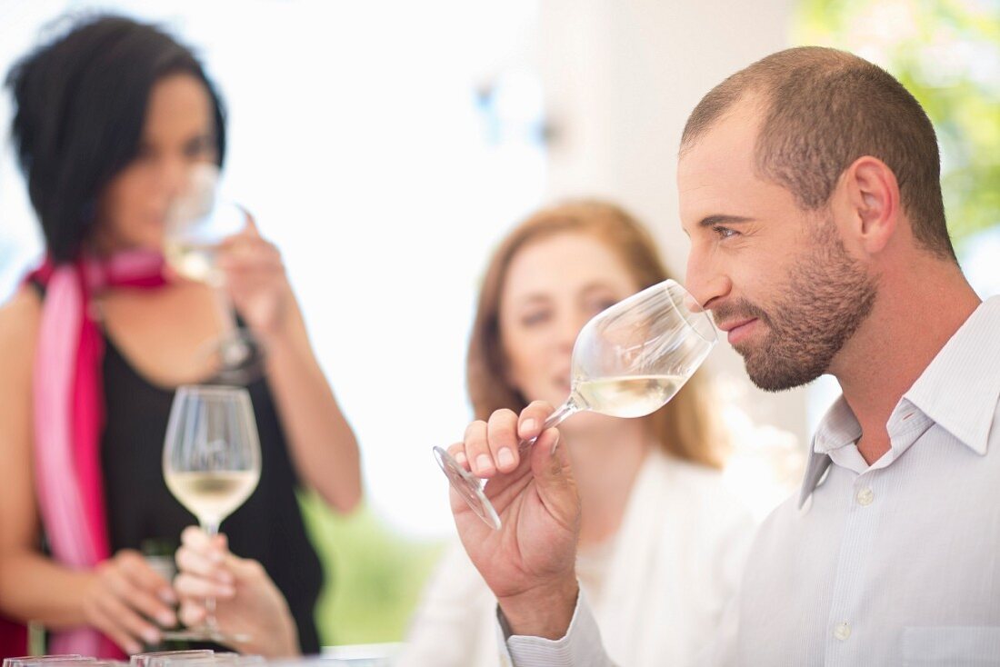 Personen bei Weinverkostung: Junger Mann riecht an Glas mit Weißwein