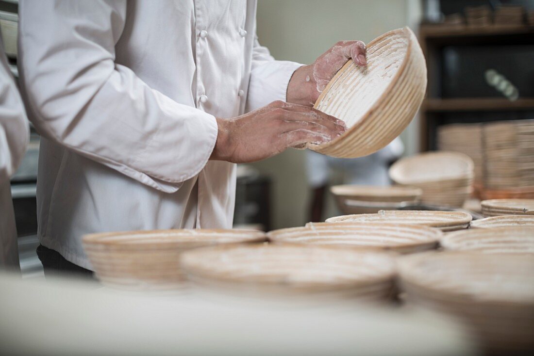 A baker dusting wicker bread baking baskets with flour