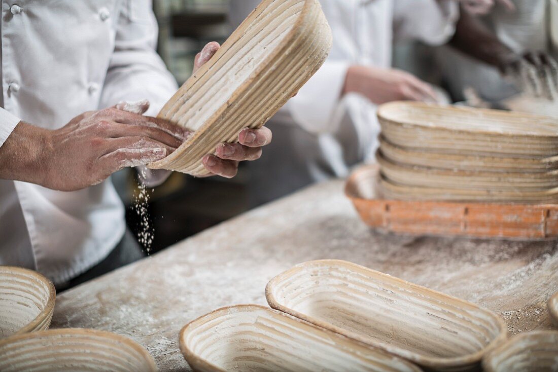 Bäcker beim Ausmehlen von Brotbackformen aus Peddigrohr