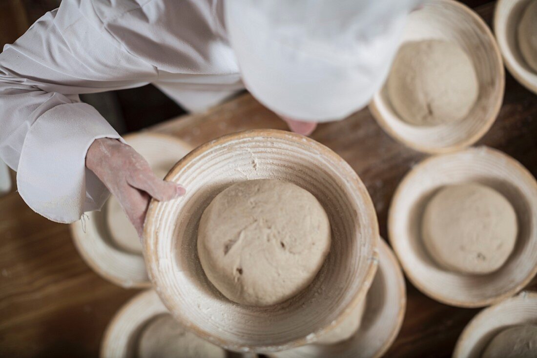 Bäcker bei der Brotherstellung: Brotteig in Brotbackformen aus Peddigrohr füllen