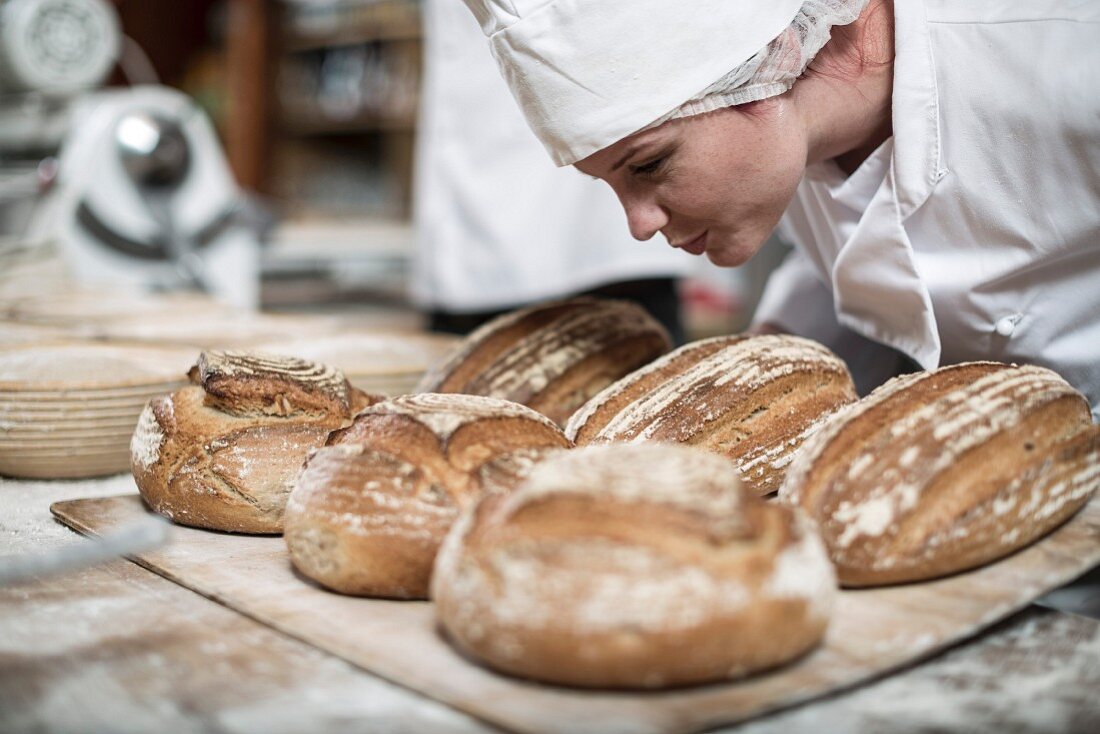 Bäckerin riecht an fertiggebackenen Brotlaiben