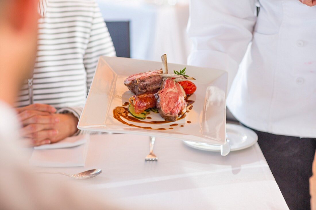 A waiter in a restaurant serving a meat dish