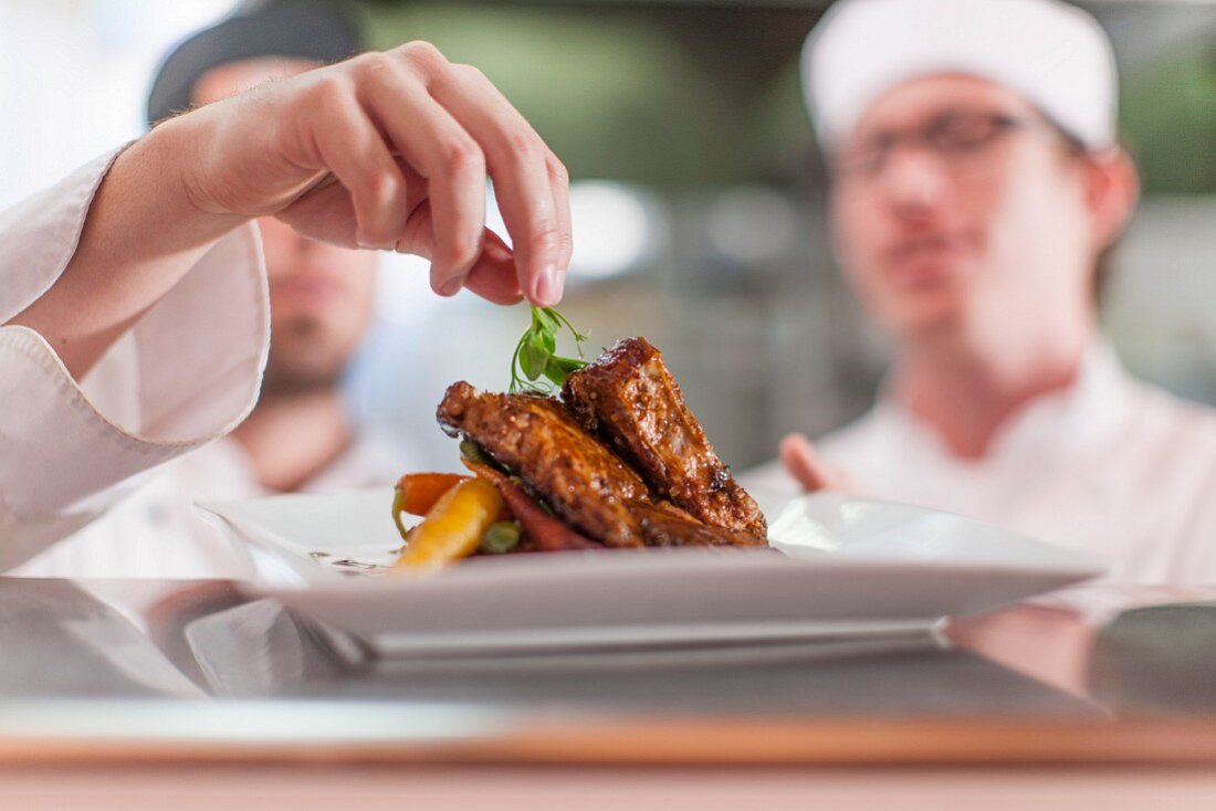 Koch in Restaurantküche garniert Fleischgericht mit Kräutern