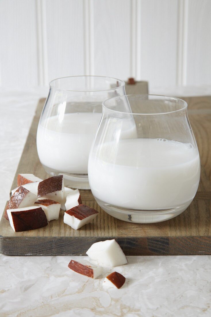 Two glasses of vegan coconut milk and pieces of coconut