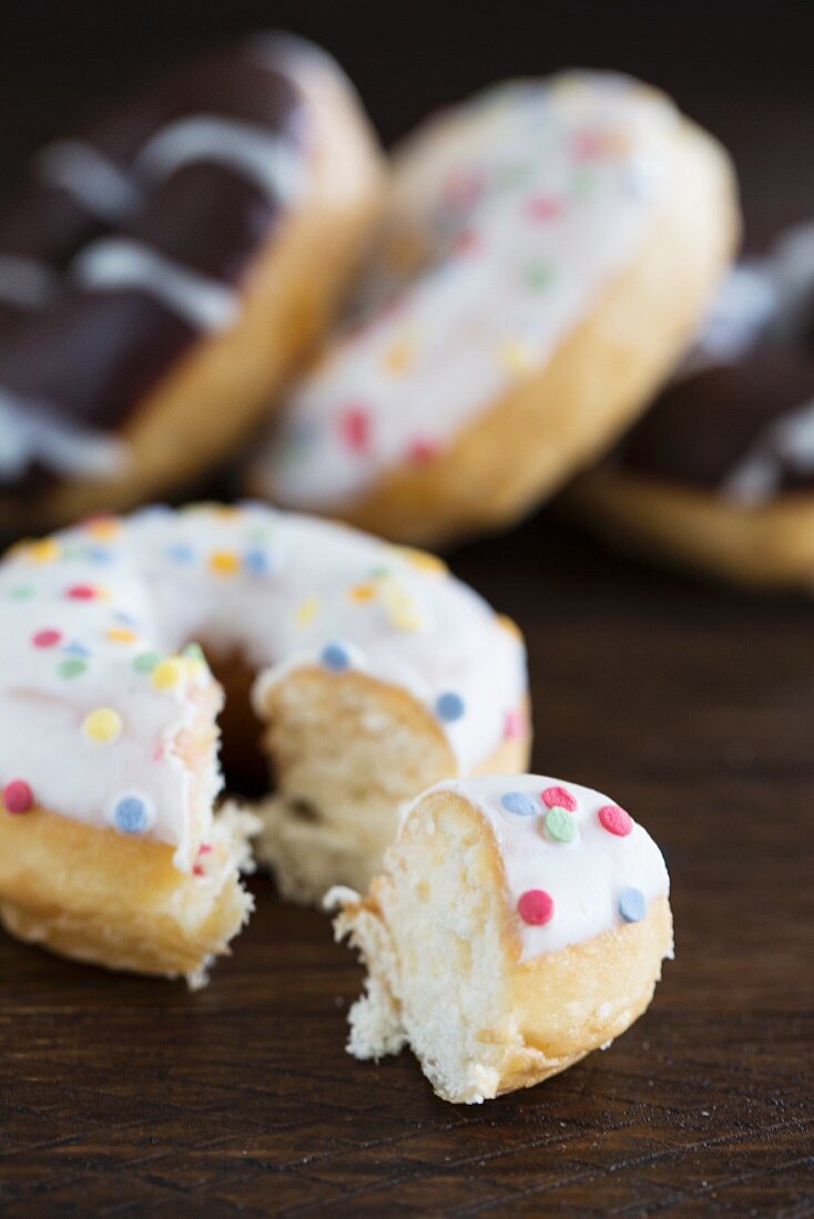 Doughnuts with various glazes on a wooden surface with one in the foreground with sugar sprinkles