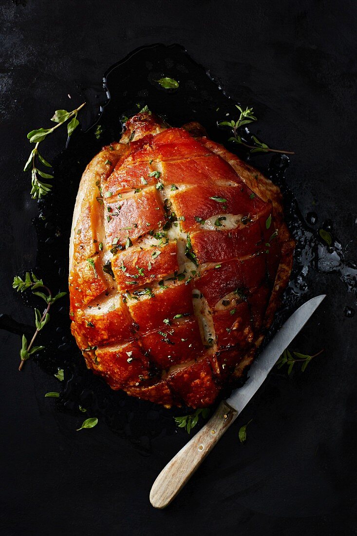 Crispy roast pork with a knife on a dark surface (seen from above)