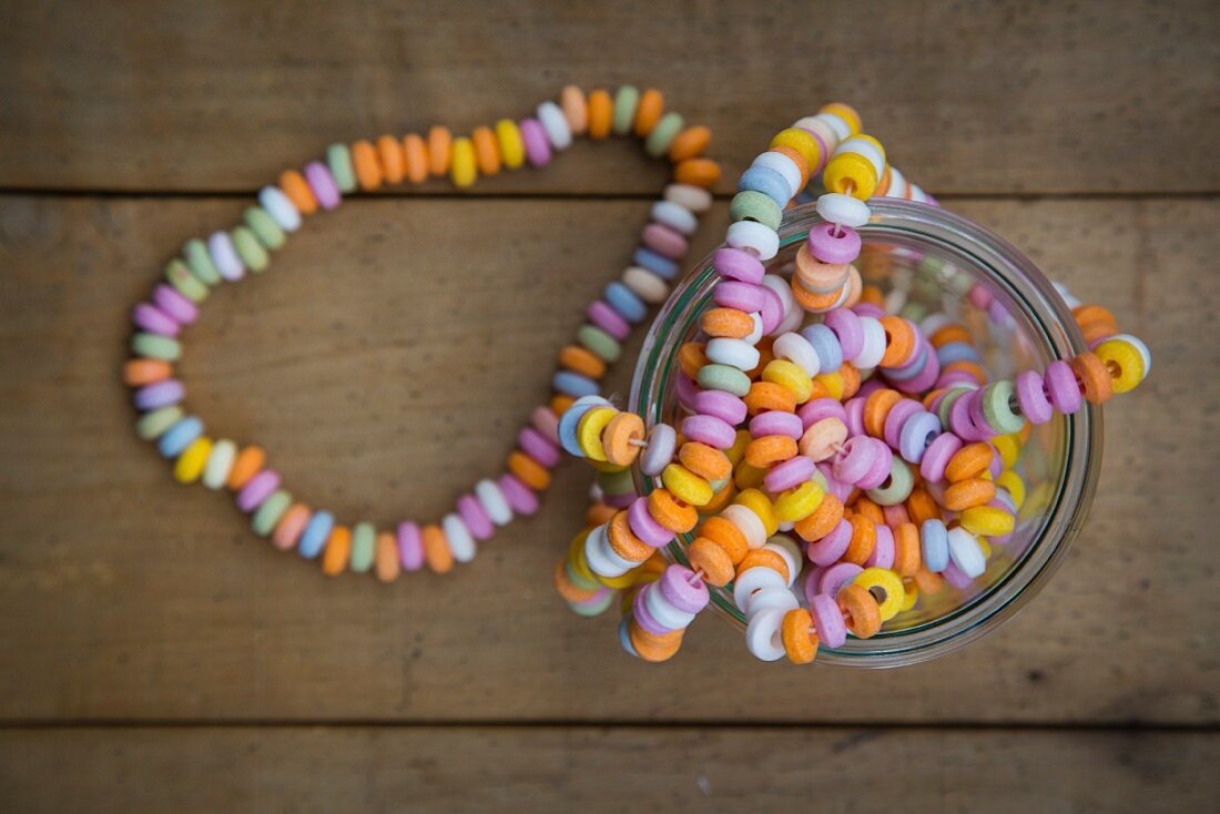 A colourful candy necklace in a jar on a wooden surface (seen from above)