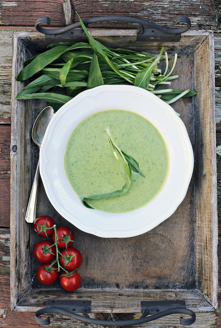 Wild garlic soup on a wooden tray with wild garlic leaves and tomatoes