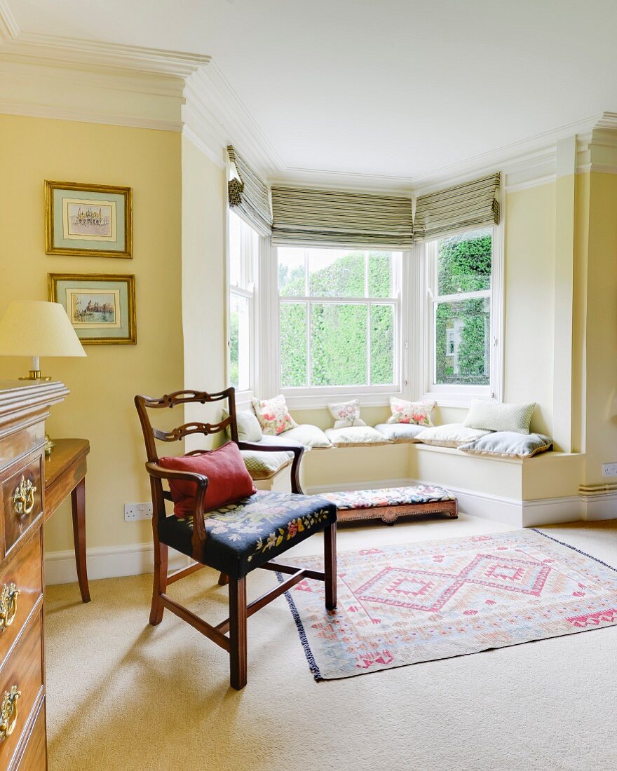 Antique armchair next to window bay with masonry window seat in yellow-painted living room