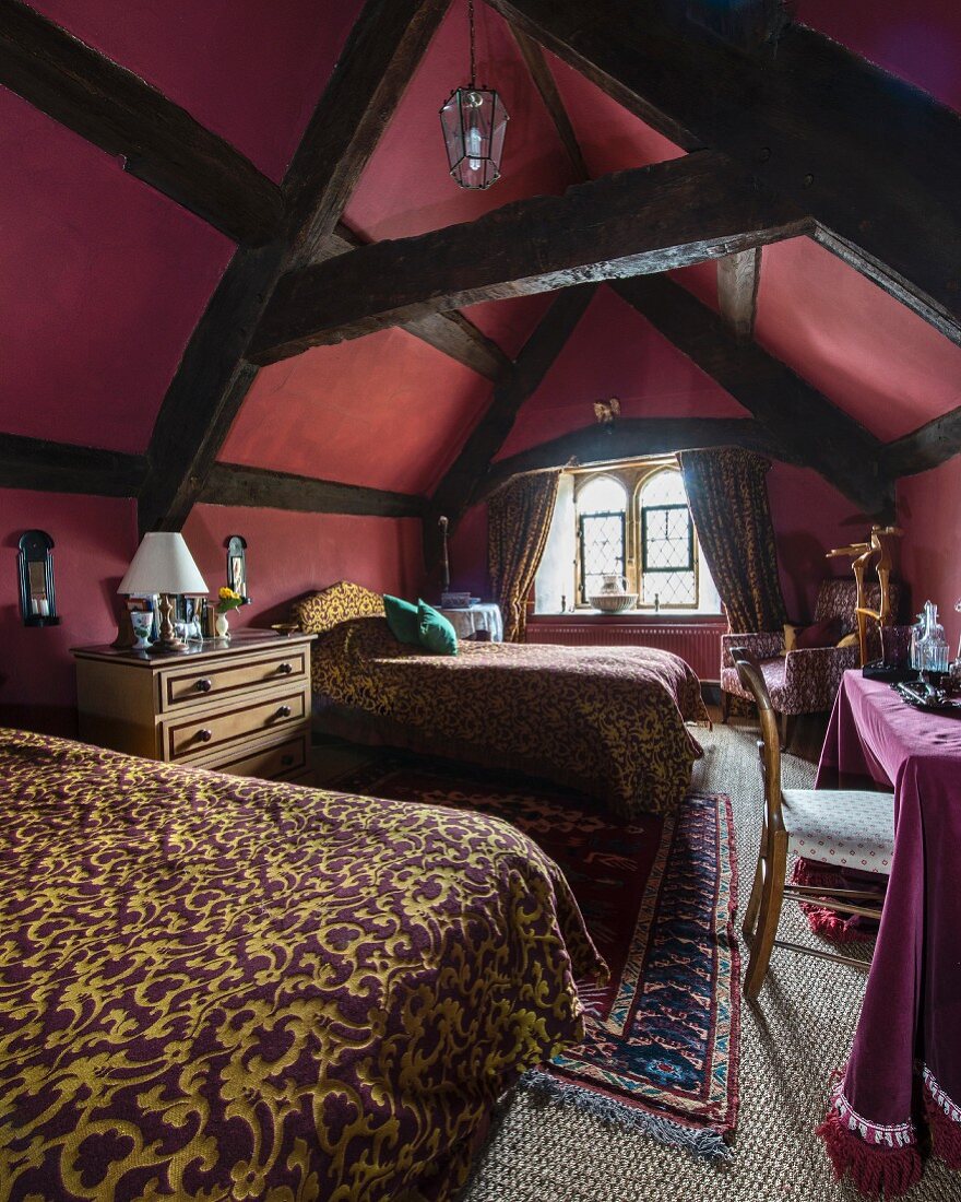 Schlafzimmer in bordeauxrot unter dunklem Holz-Dachstuhl, Betten mit elegantem Überwurf
