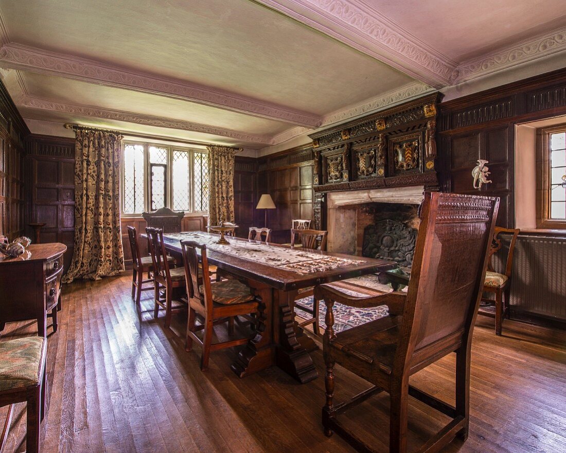 Open fireplace and wooden chairs around long dining table in grand dining room