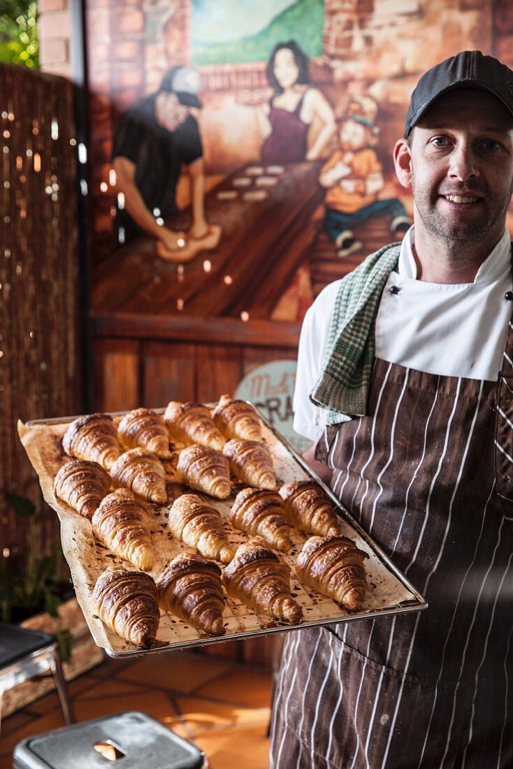 Young pastry chef with fresh croissants on a baking tray