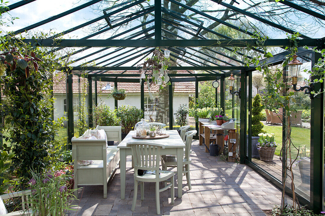 Table and seating in large conservatory in spring garden
