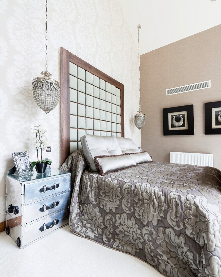 Bedspread with ornamental pattern on double bed with tall headboard against wall in corner of elegant bedroom