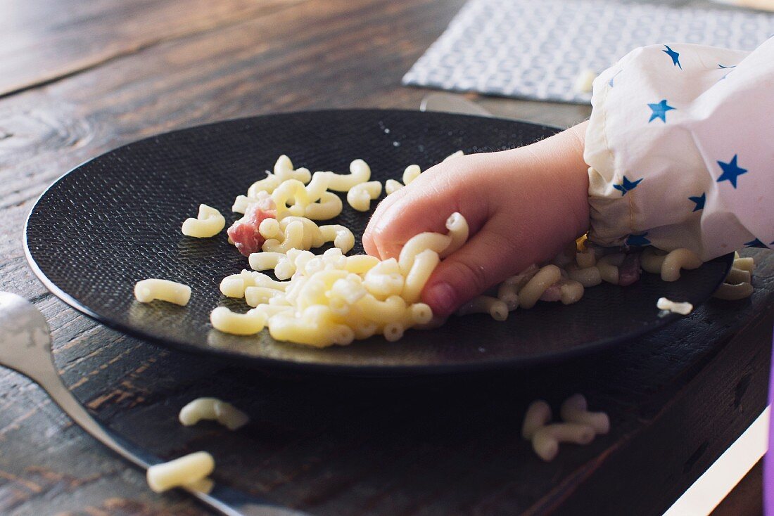 Kinderhand greift nach gekochten Nudeln